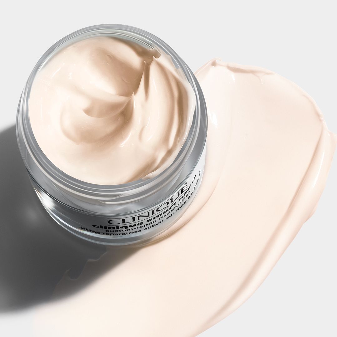 Glasbehälter mit Creme und cremiger Textur. Auf einer hellen Oberfläche. Text: CLINIQUE.