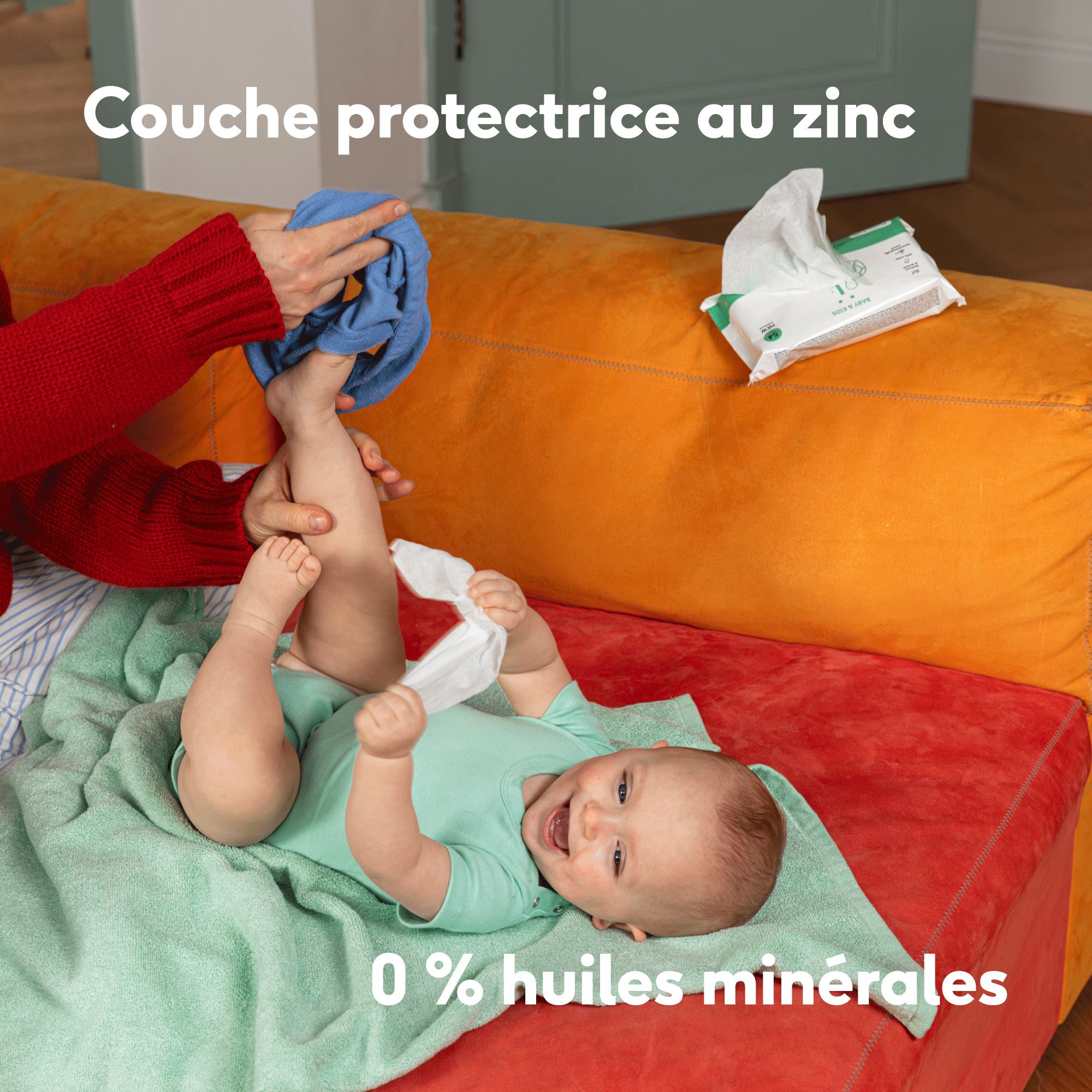 Bébé est changé. Texte: Couche protectrice au zinc. 0% huiles minérales. Fond: Canapé orange.