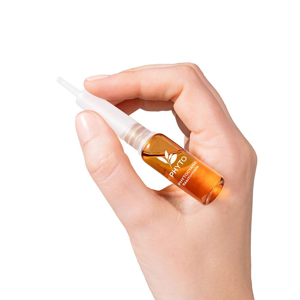 Main tenant une ampoule ambrée. Inscription: Phyto Phytocyane.
