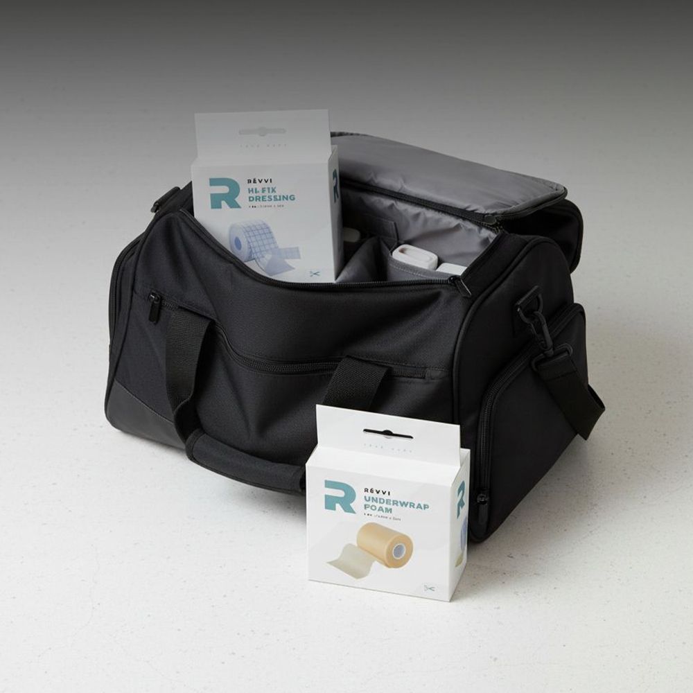 Sac de sport noir, partiellement ouvert. Deux emballages RÉVVI Underwrap Foam. Image du produit visible.