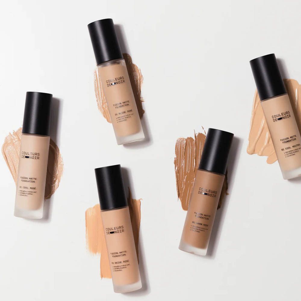 Plusieurs flacons de fond de teint. Inscription : COULEURS DE NOIR, FUSION MATTE FOUNDATION. Différentes teintes.