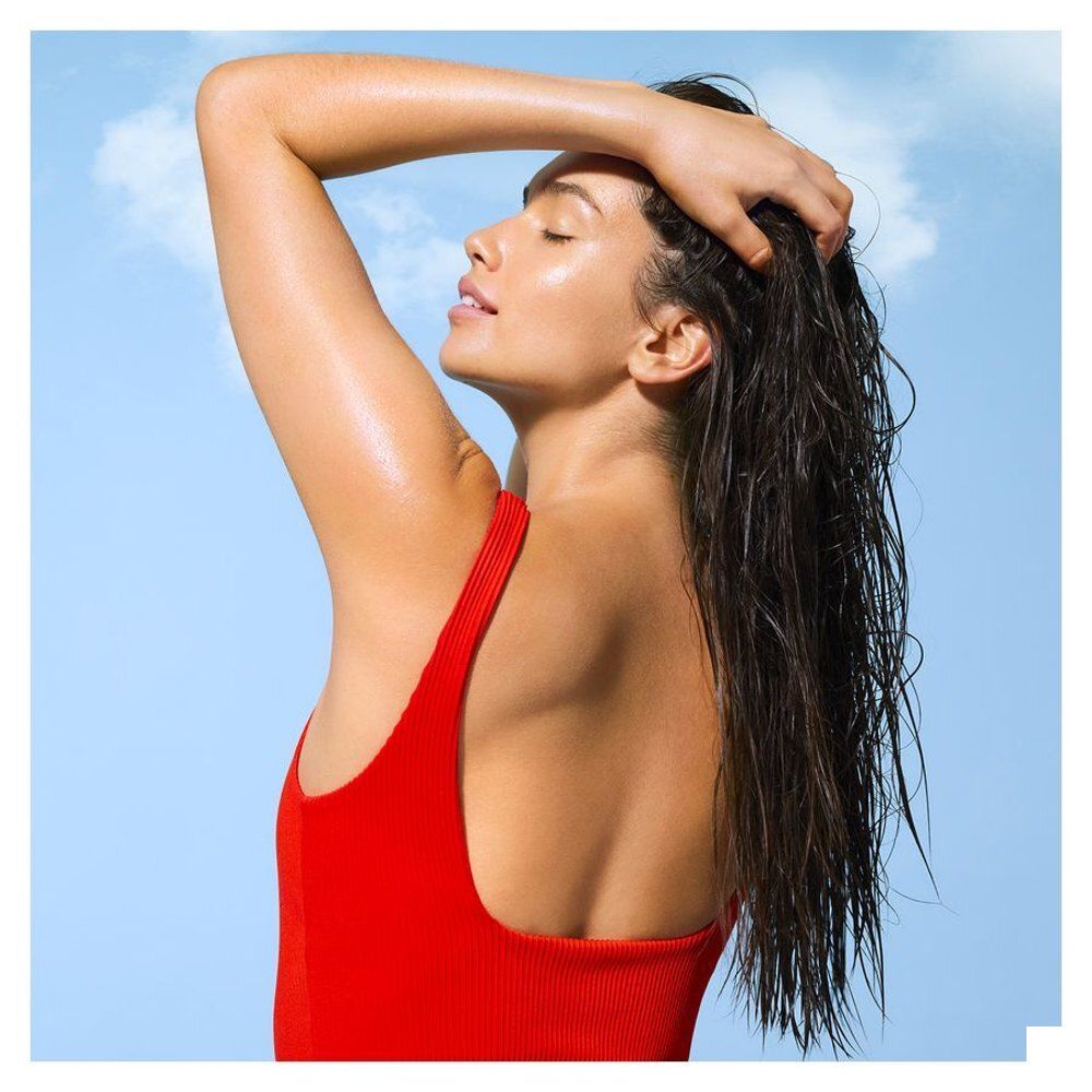 Femme aux cheveux mouillés en maillot de bain rouge devant un ciel bleu.