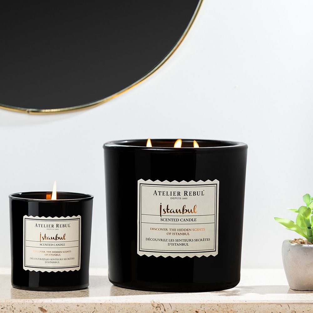 Zwei schwarze Kerzen. Aufkleber mit Text: Atelier Rebul Istanbul Scented Candle. Eine brennt.