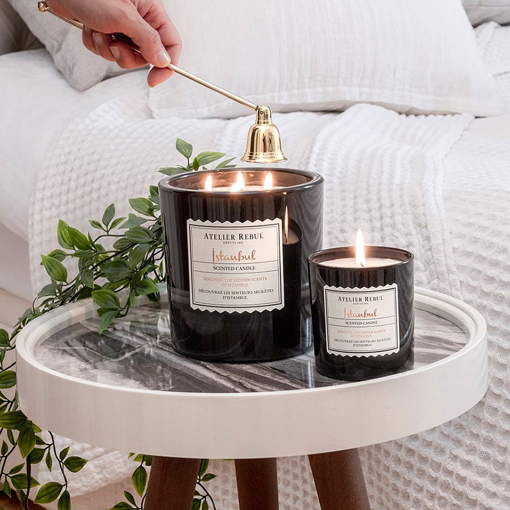 Zwei schwarze Kerzen brennen. Aufkleber mit Text: Atelier Rebul Istanbul Scented Candle. Goldene Glocke.