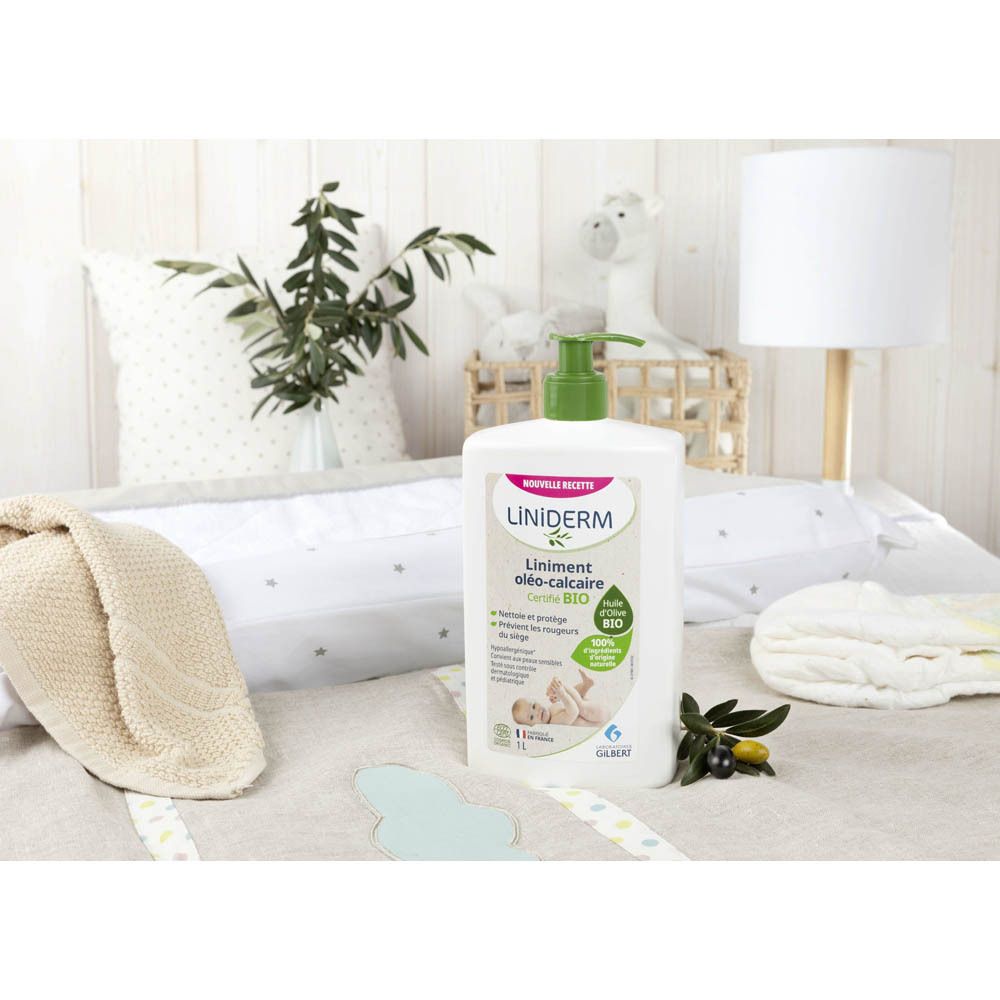 Flacon blanc avec pompe verte sur une table à langer. Environnement: oreillers, couverture, jouets. Inscription: Liniderm.