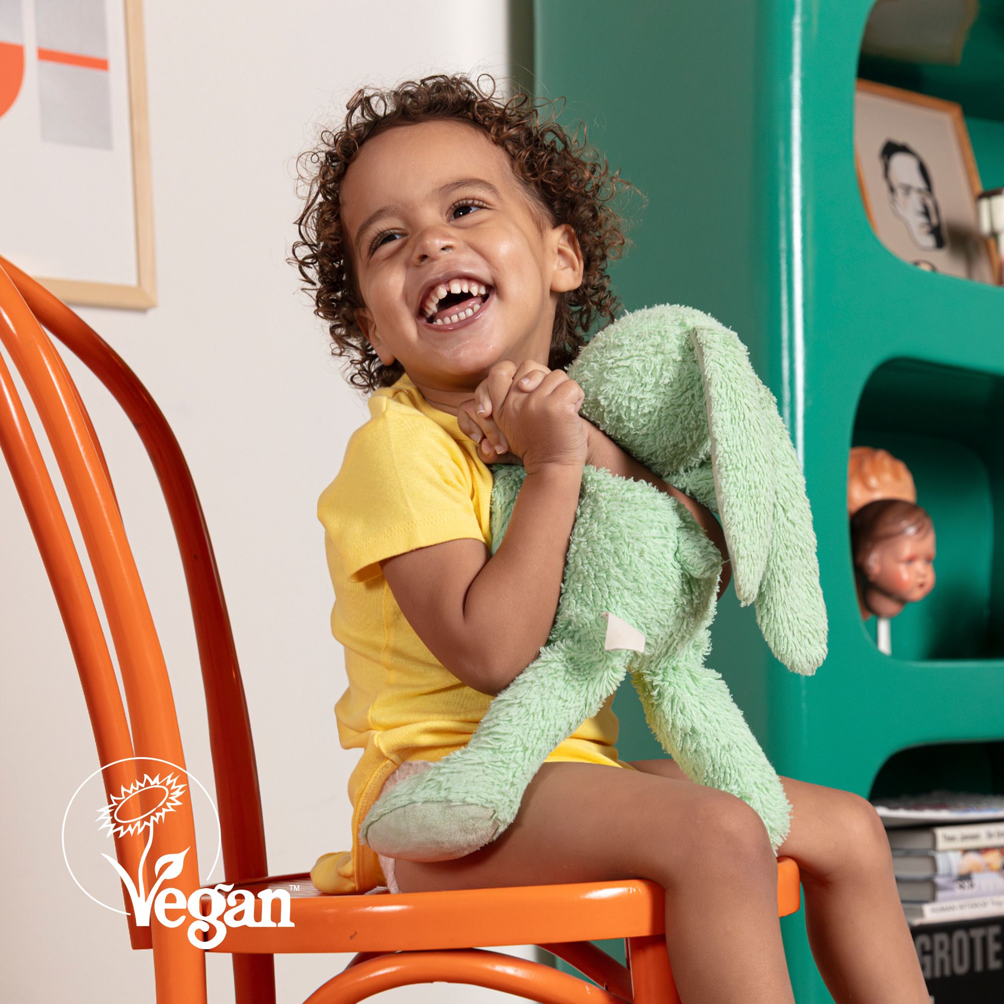 Enfant avec une peluche verte. Logo végan.