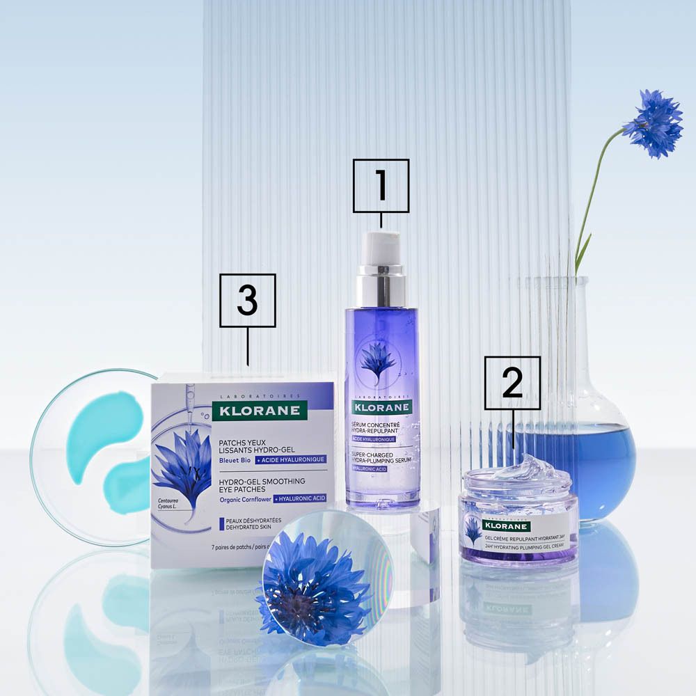Arrangement produits: patchs yeux, sérum, crème Klorane. Fleurs bleues, flacons.