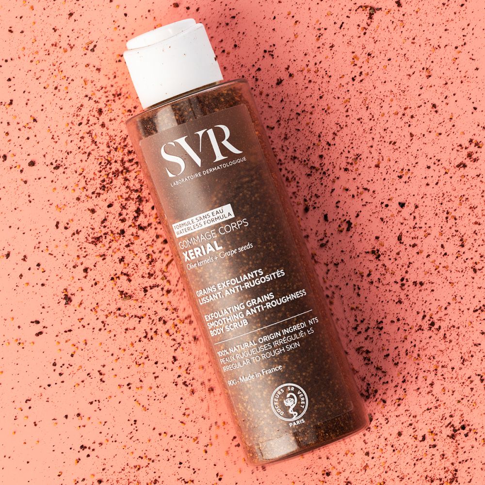 Flacon et gommage sur fond rose. Gommage dispersé. Inscription SVR, Gommage Corps Xerial.