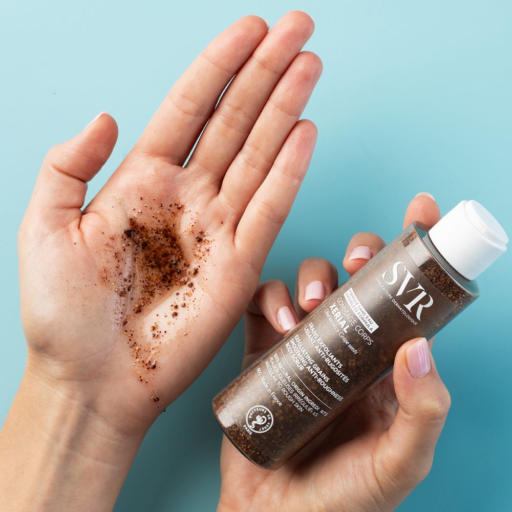 Mains avec gommage. Flacon avec inscription SVR, Gommage Corps Xerial. Gommage brun sur main.