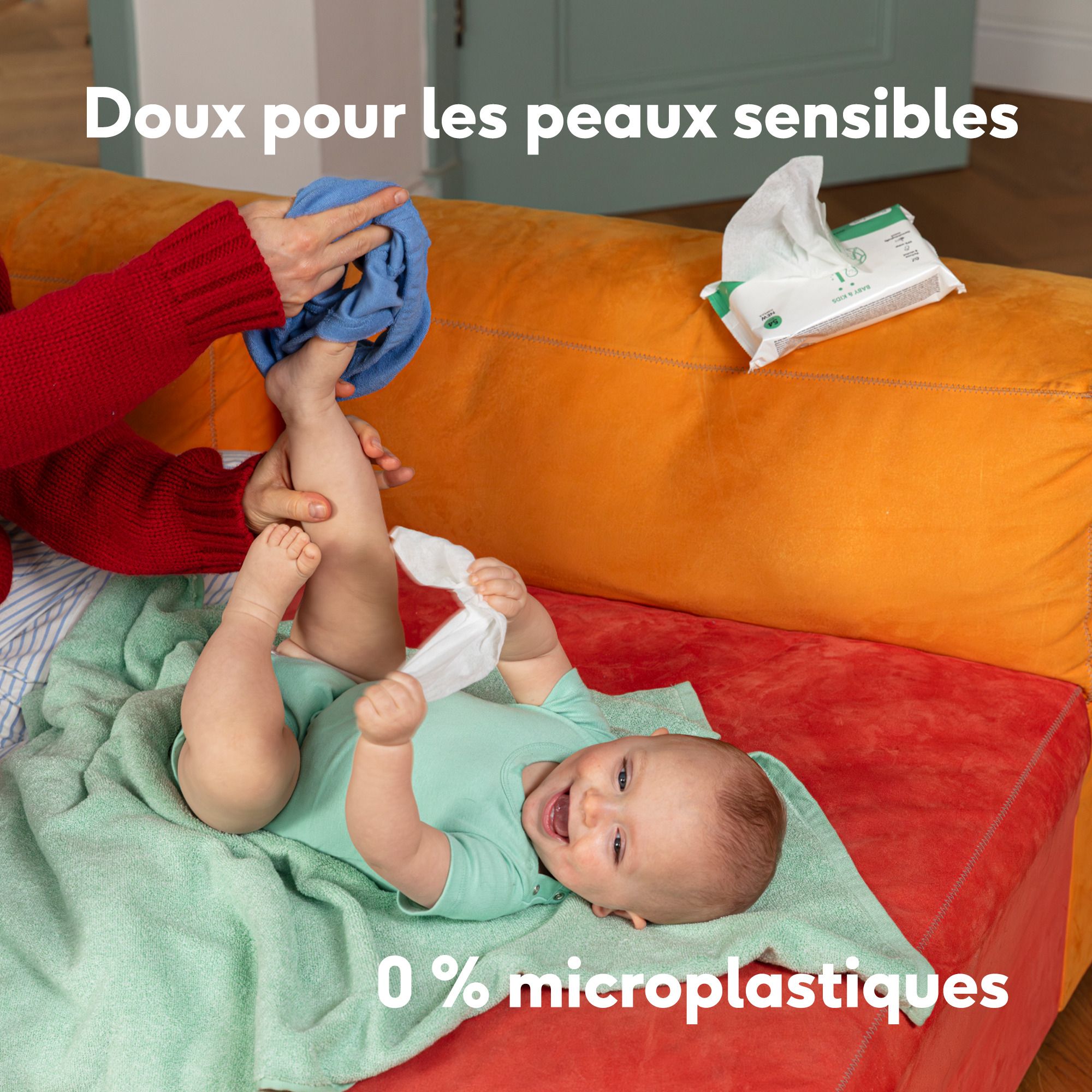 Bébé sur une couverture, une main nettoie les pieds. Texte : 0% microplastiques.