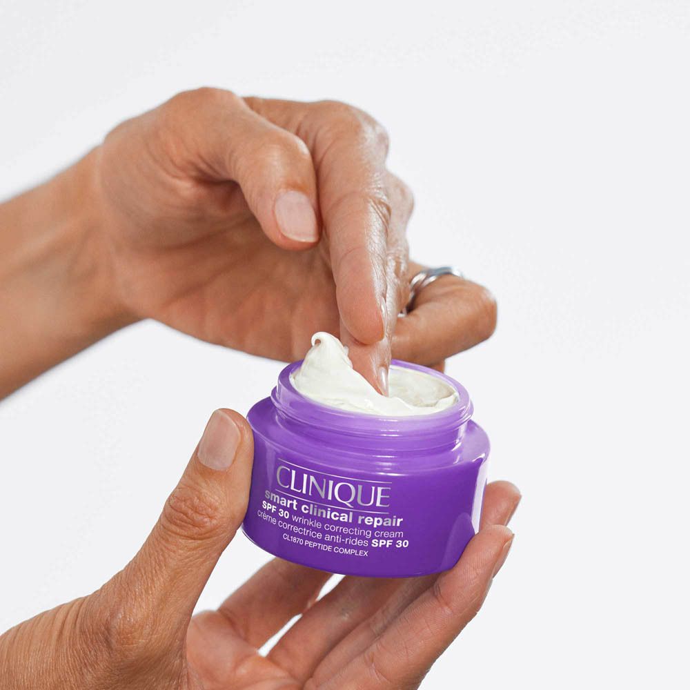 Eine Hand öffnet einen violetten Tiegel mit Clinique Smart Clinical Repair Feuchtigkeitscreme SPF 30.