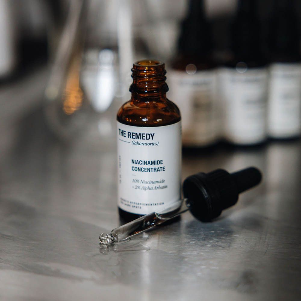 Hände halten eine Flasche 'THE REMEDY NIACINAMIDE CONCENTRATE' mit Pipette.
