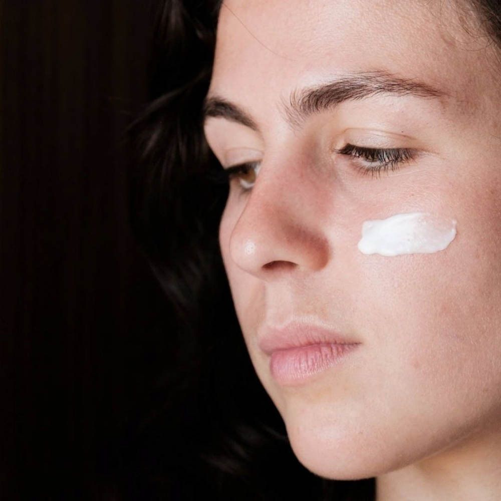 Femme avec crème sur la peau. Crème appliquée sur la joue. Fond sombre.