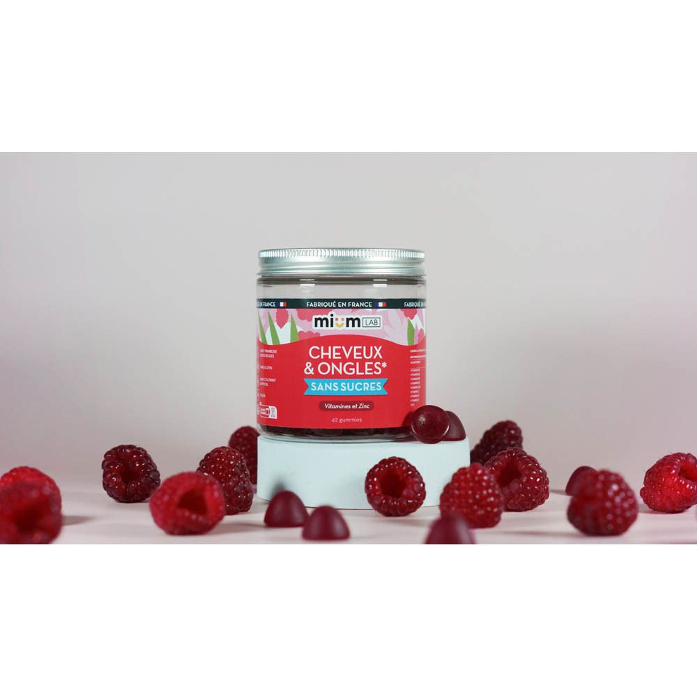 Glasbehälter mit Mium Lab Magnesium Gummis, zuckerfrei, umgeben von Himbeeren.