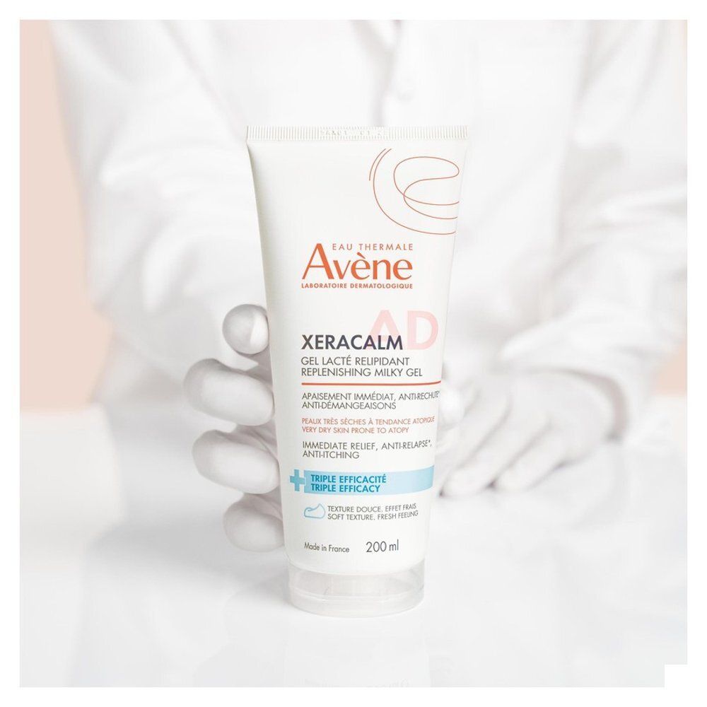 Personne tenant un tube. Texte: XeraCalm AD, 200 ml. Mains gantées. Arrière-plan flou.