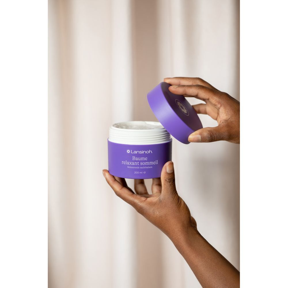 Hände öffnen lila Tiegel. Weißes Produkt sichtbar. Text: Lansinoh, Baume relaxant sommeil, 200 ml.