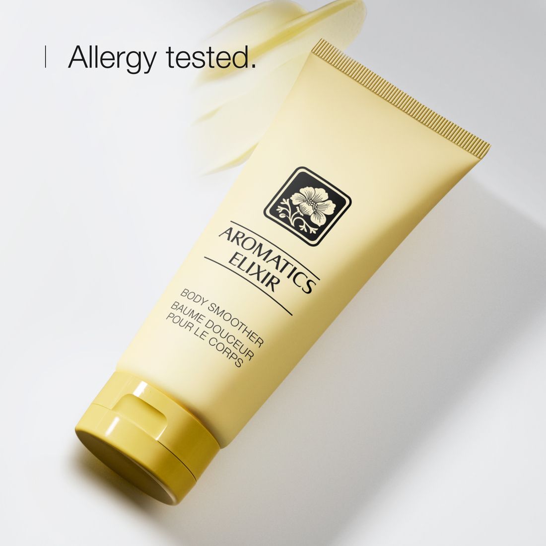 Tube avec contenu jaune. Texte : Aromatics Elixir, Body Smoother. Avec fleur. Fond blanc.