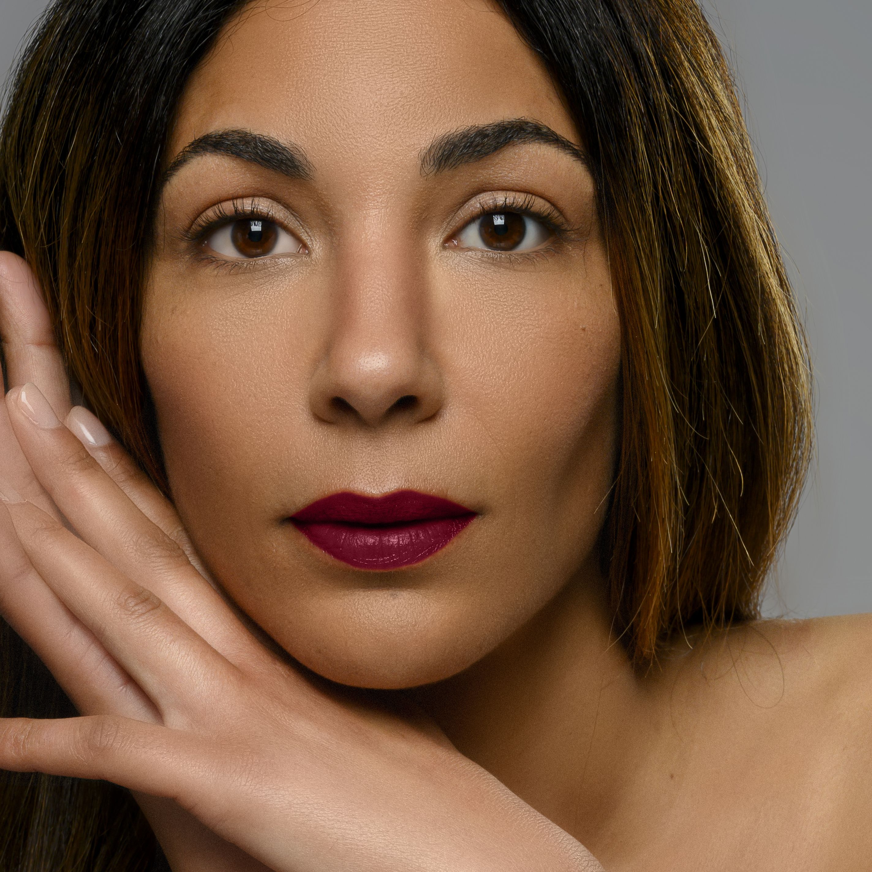 Portrait d'une femme avec rouge à lèvres bordeaux. Mains sur le visage.