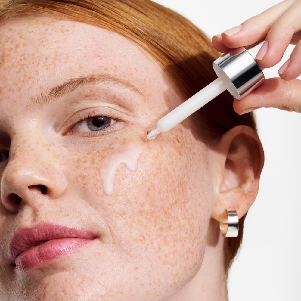 Femme avec compte-gouttes sur la peau. Goutte de sérum sur la joue. Cheveux roux.