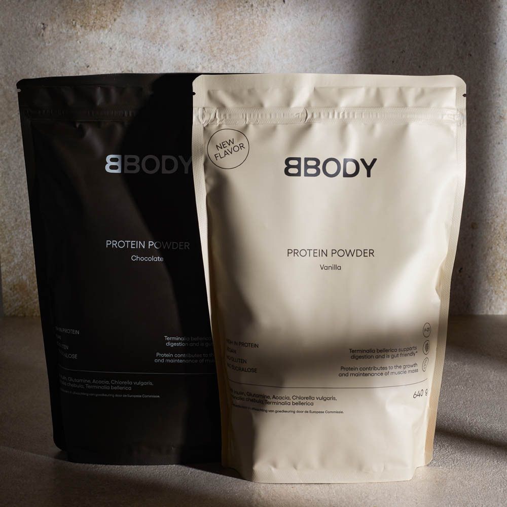 Deux sachets BBODY Protein Powder, Chocolat et Vanille. Texte : New Flavor, 640g. Sur une table. Sachet noir et beige.