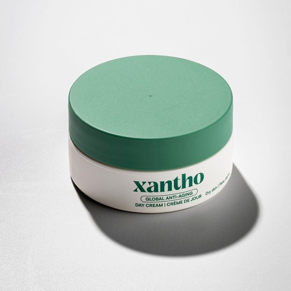Crème de jour globale anti-âge Xantho dans un pot blanc avec un couvercle vert.