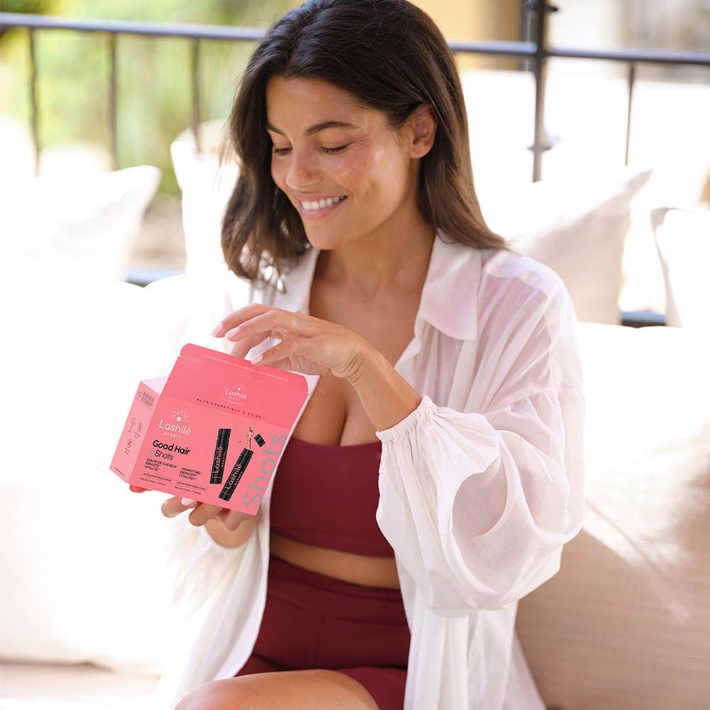 Femme tenant un paquet de Good Hair Shots. Elle sourit et est à l'extérieur.