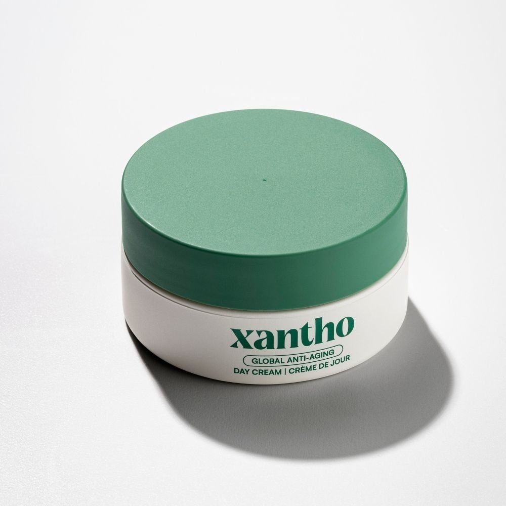 Crème de jour globale anti-âge Xantho dans un pot blanc avec couvercle vert.