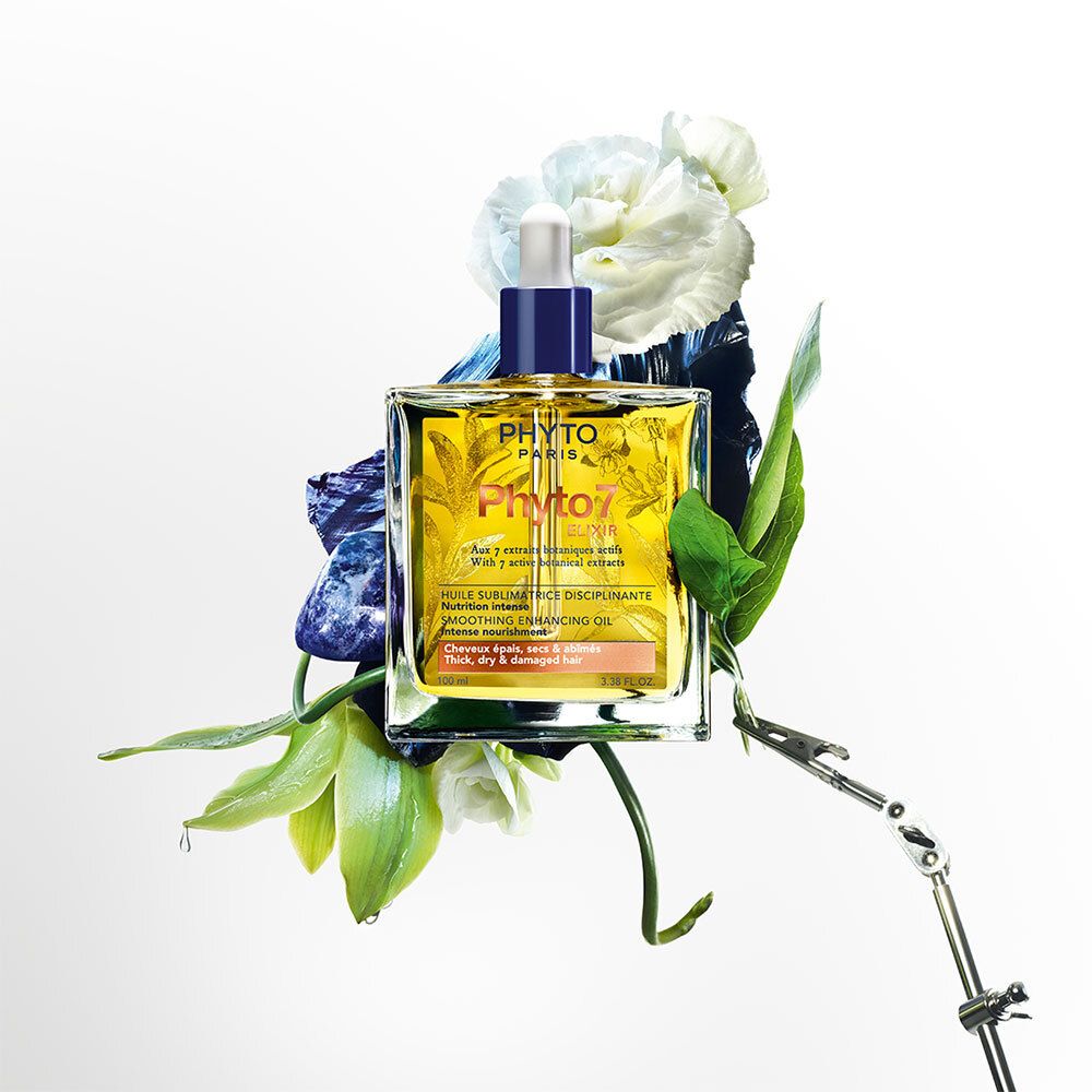 Quadratische Glasflasche mit gelbem Öl, umgeben von Blumen und Blättern. Aufschrift: Phyto Paris, Phyto7 Elixir. Mit Tropfer.