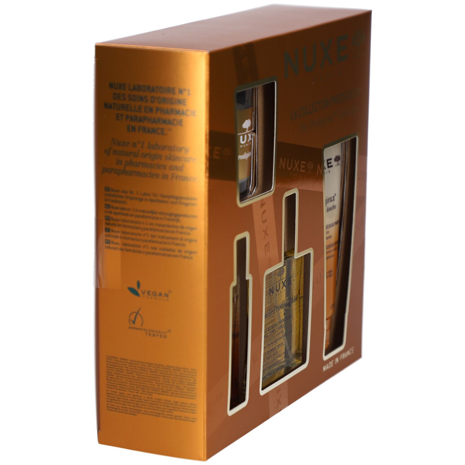 Goldfarbene Geschenkbox mit Produkten. Rückseite mit Text und Vegan-Logo. Markenname Nuxe.
