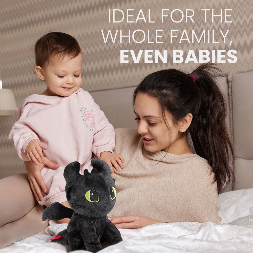 Schwarzer Plüsch-Drache mit Baby und Frau auf einem Bett.