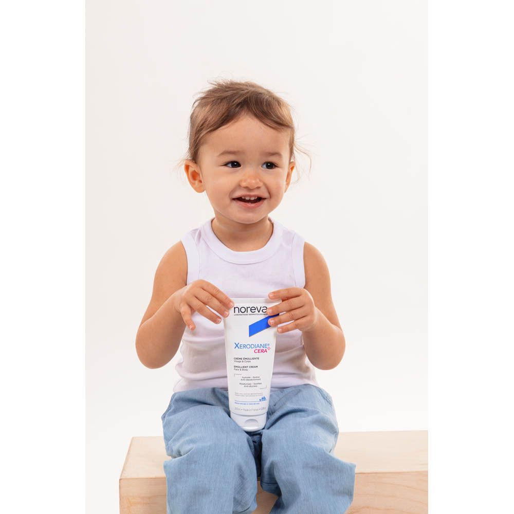 Kind hält eine Noreva Xerodiane Cera Emollient Cream Flasche.