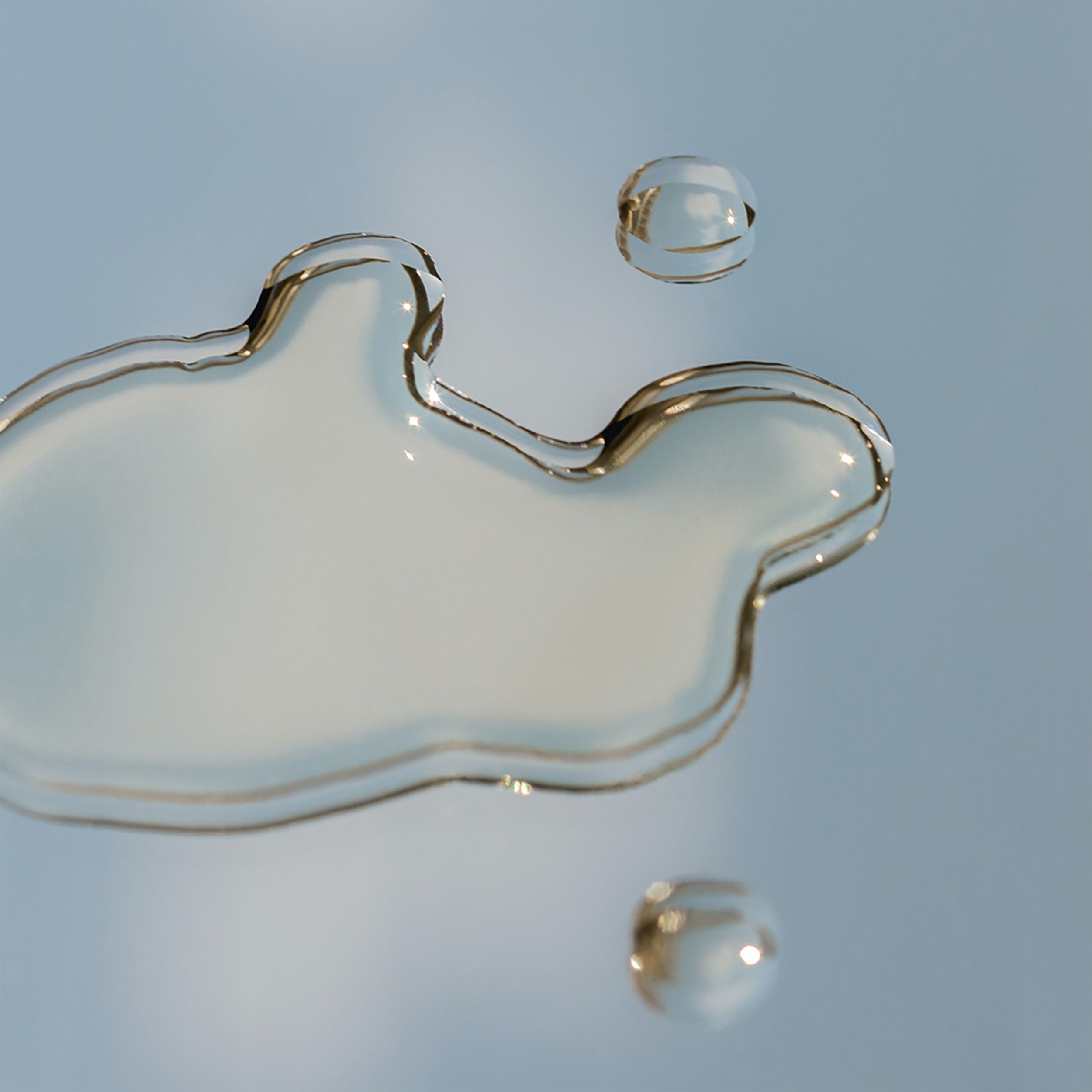 Trois gouttes de liquide sur une surface bleu clair. Formes rondes et irrégulières. Liquide transparent.