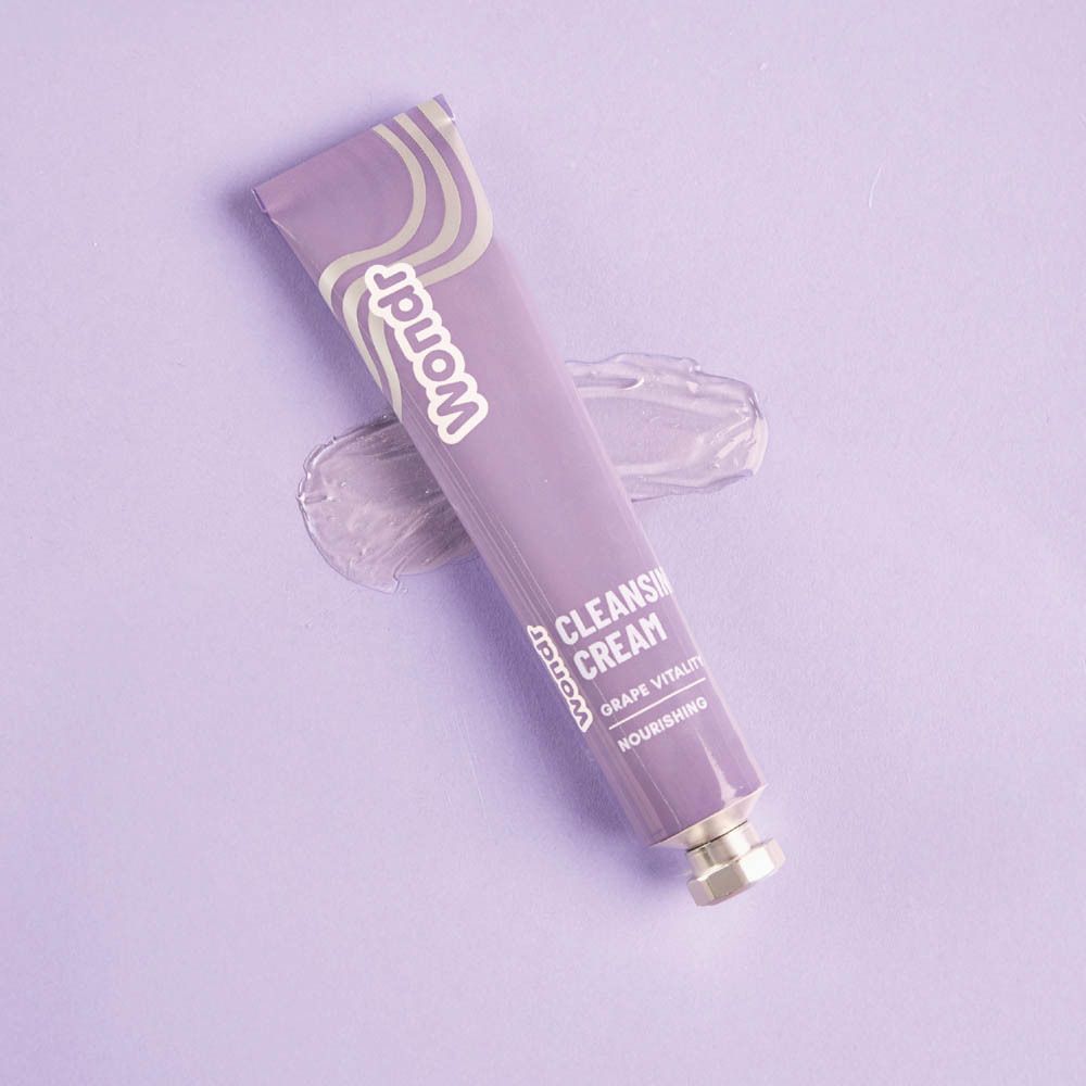 Tube violet avec logo "Wondr" et texte "Cleansing Cream Grape Vitality". Sur fond violet avec une goutte de crème.