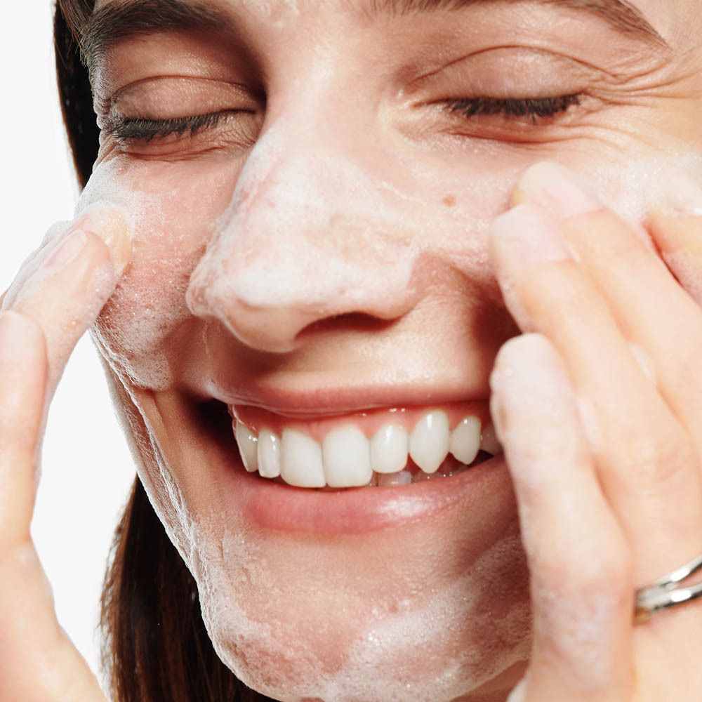 Frau mit geschlossenen Augen wendet Schaum auf ihr Gesicht an.