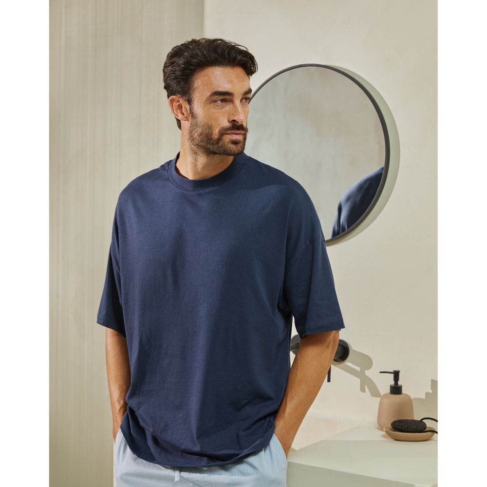 Homme dans une salle de bain, souriant. Porte un t-shirt bleu, miroir en arrière-plan.