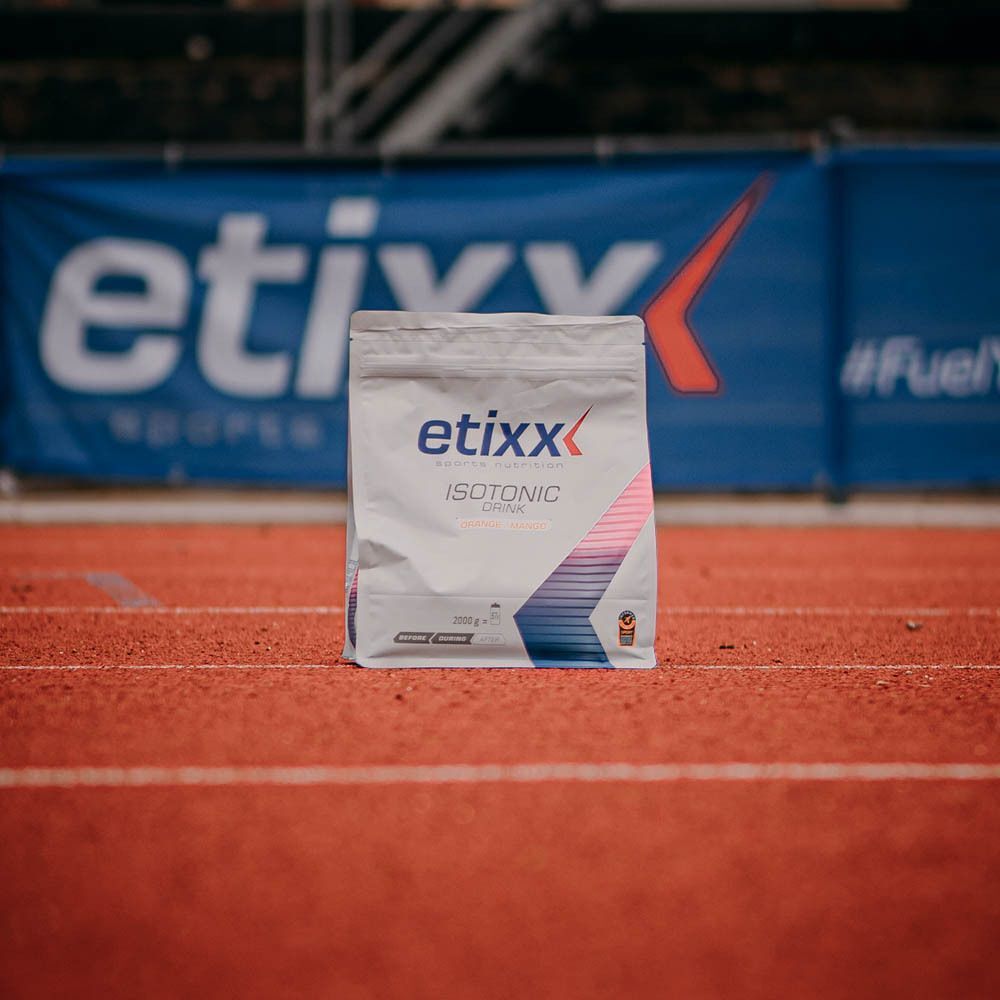 Ein Beutel Etixx Isotonic Drink Orange-Mango auf einer Laufbahn mit Etixx-Banner im Hintergrund.
