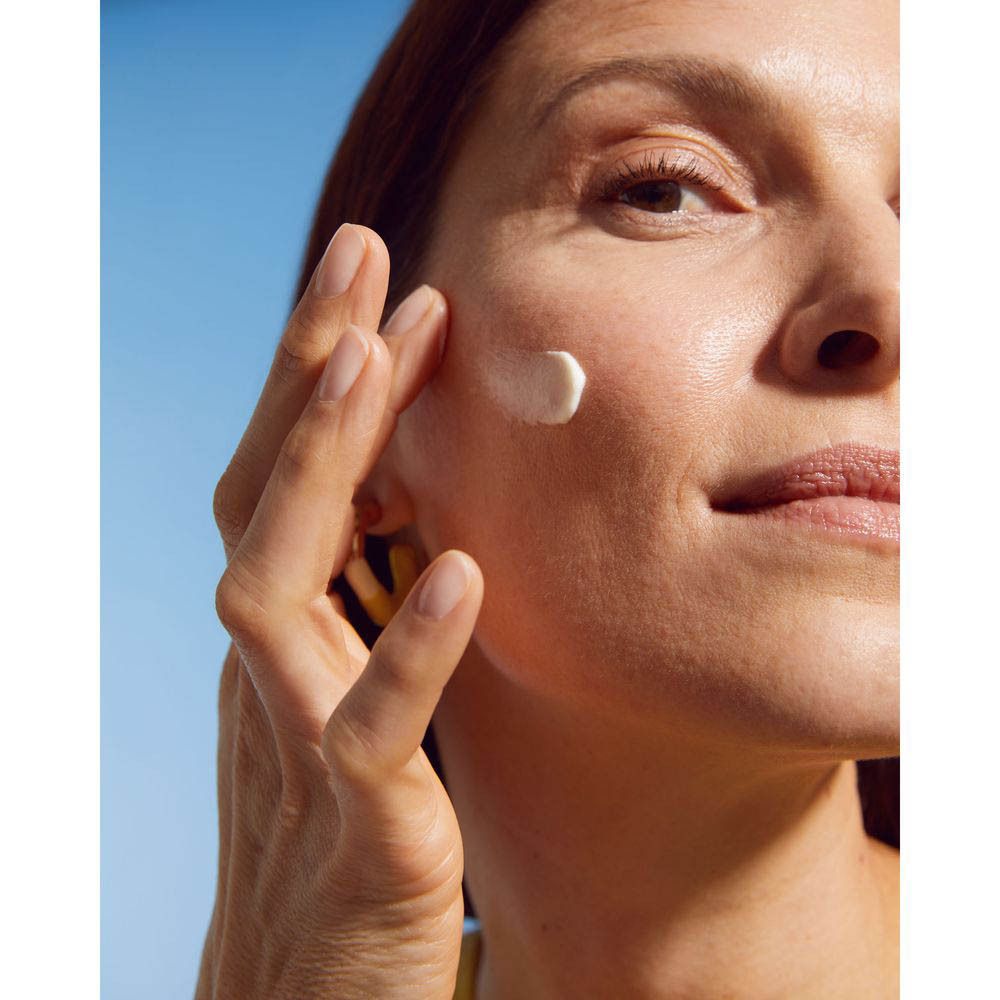 Femme à la peau lisse touchant son visage, devant un ciel bleu.