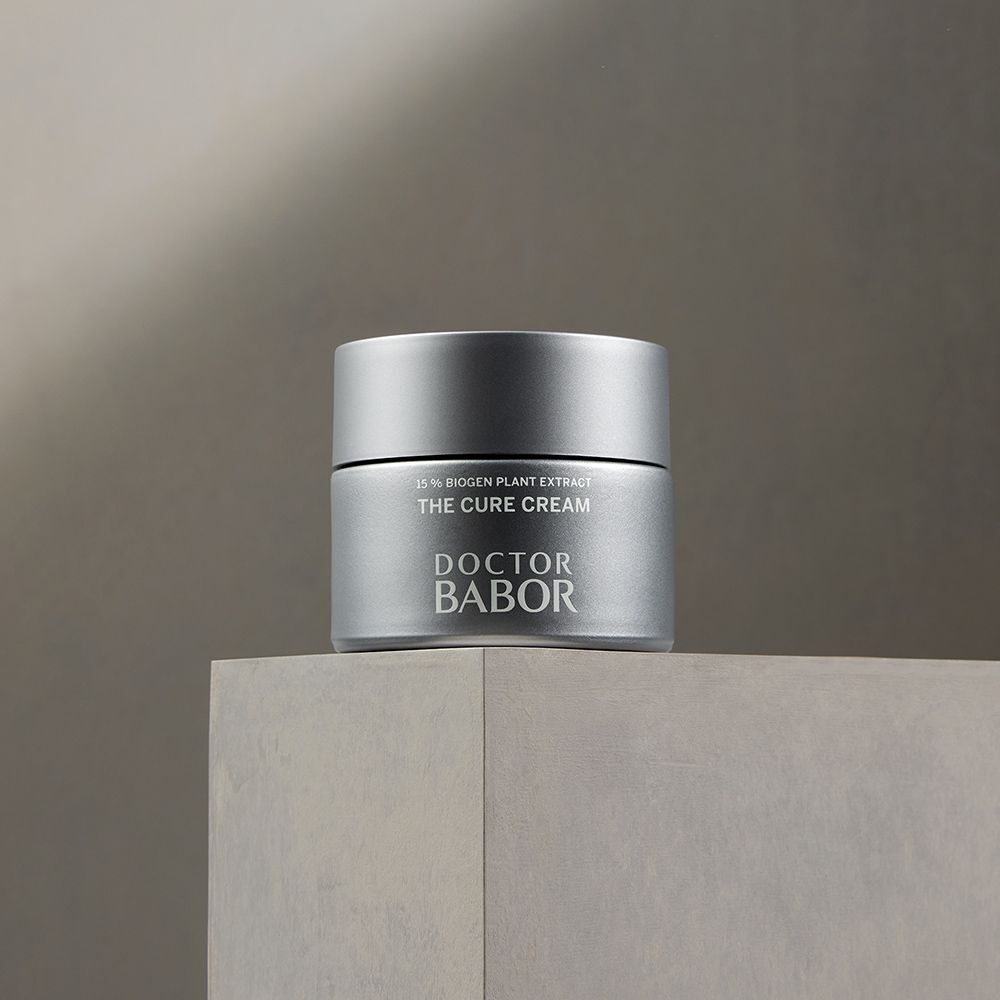 Silberfarbener Creme-Tiegel auf einer grauen Oberfläche. Aufschrift: THE CURE CREAM, DOCTOR BABOR.