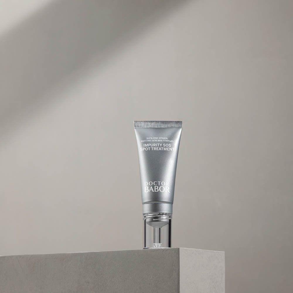 Tube argenté avec applicateur transparent sur un socle. Inscription : Impurity SOS Spot Treatment, Doctor Babor.