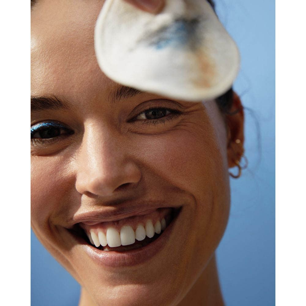 Femme tenant un coton démaquillant avec des restes de maquillage devant son œil. Nivea Skin Glow Eau Micellaire.