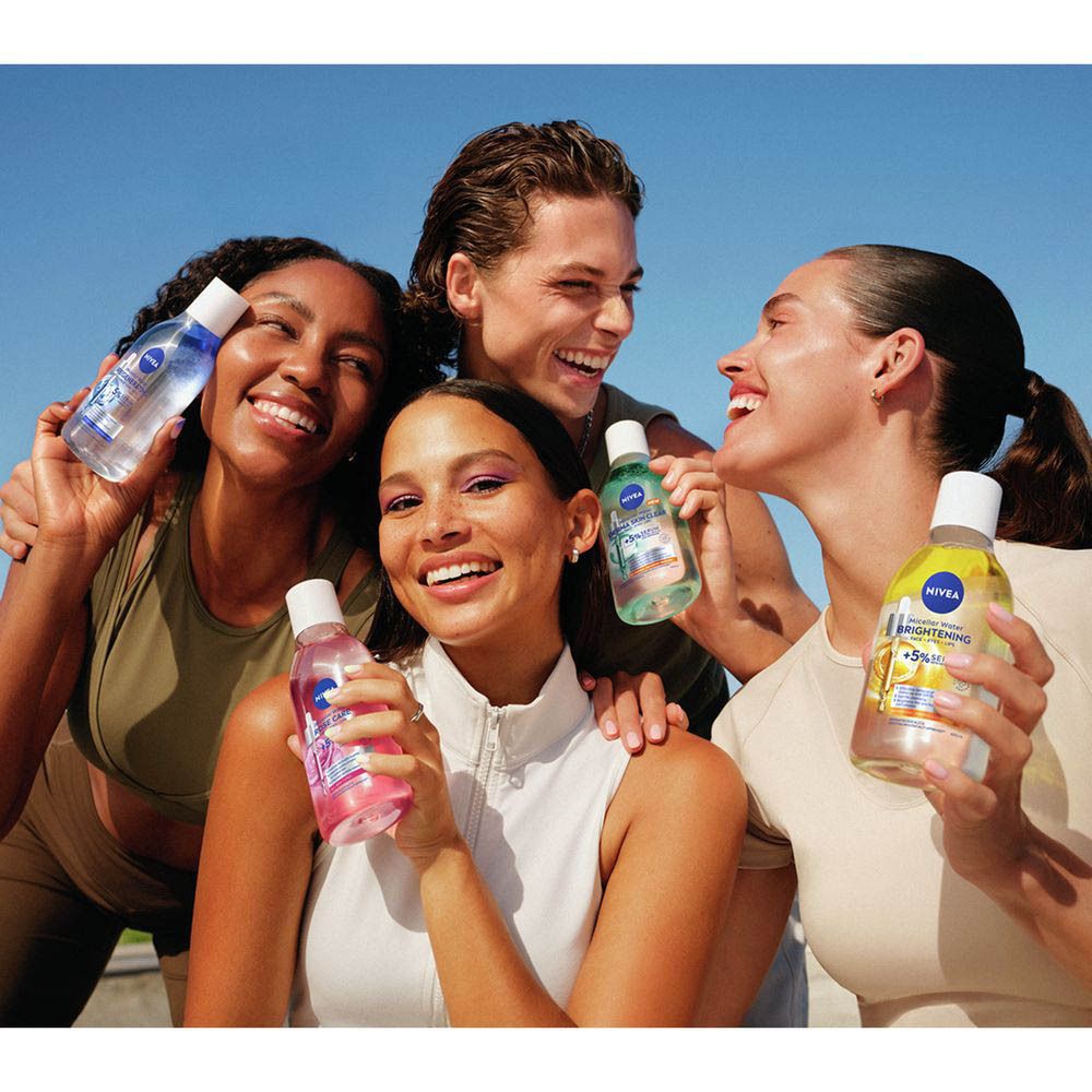 Quatre jeunes adultes souriants tiennent des bouteilles de Nivea Skin Glow Eau Micellaire dans leurs mains.