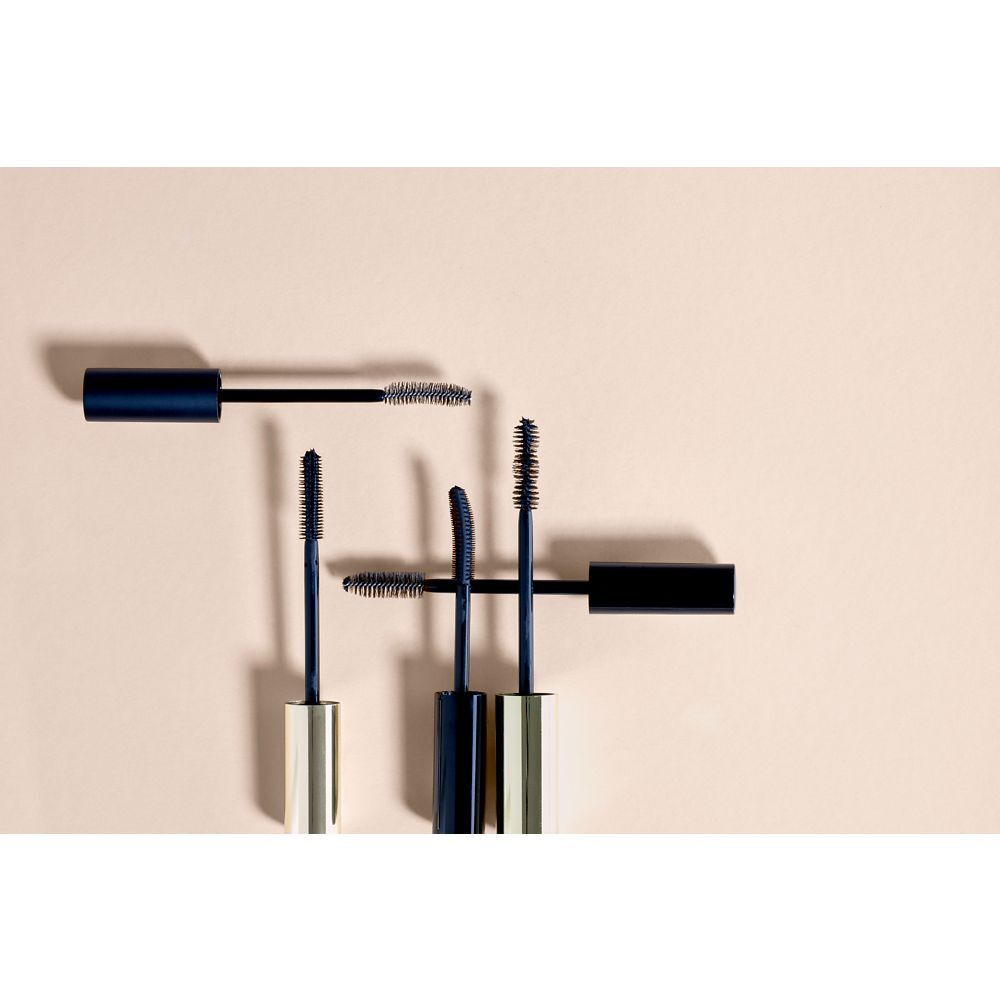 Plusieurs brosses de mascara sur fond beige. Brosses noires avec manches dorés et noirs.