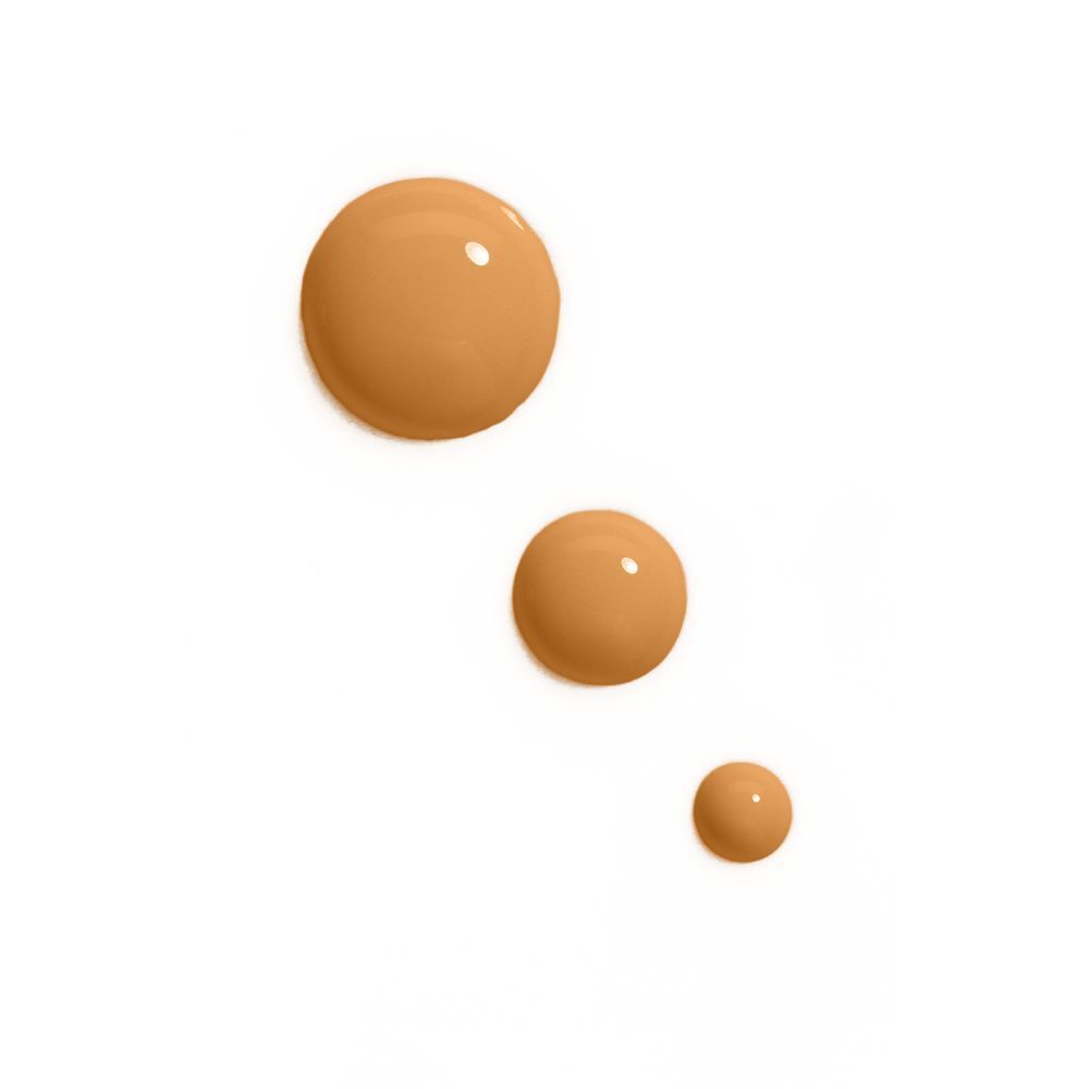 Trois gouttes de fond de teint de différentes teintes brunes sur fond blanc.