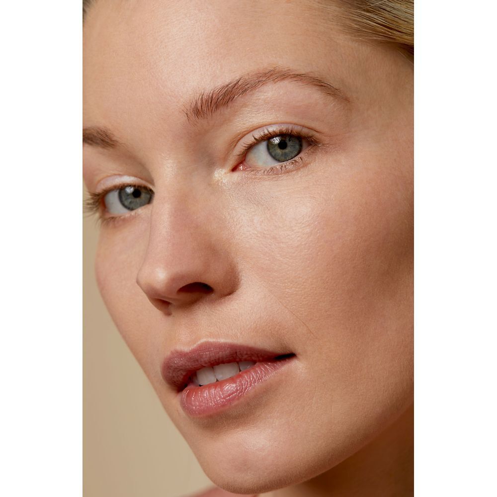 Nahaufnahme eines Gesichts. Hautton gleichmäßig, Augen blau, Lippen leicht geschminkt.