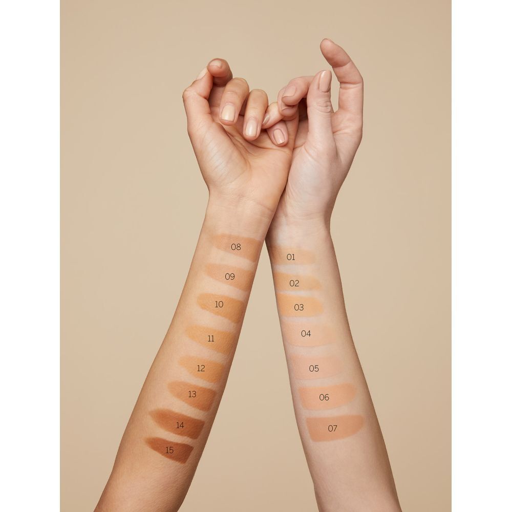 Arme mit Foundation-Farbmustern. Farbnummern 08-15 auf einem Arm, 01-07 auf dem anderen. Hintergrund beige.