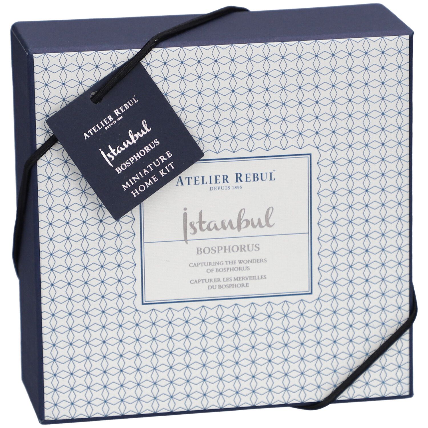 Dunkelblaue Schachtel mit weißem Muster und schwarzem Band. Anhänger mit Logo und Produktnamen.