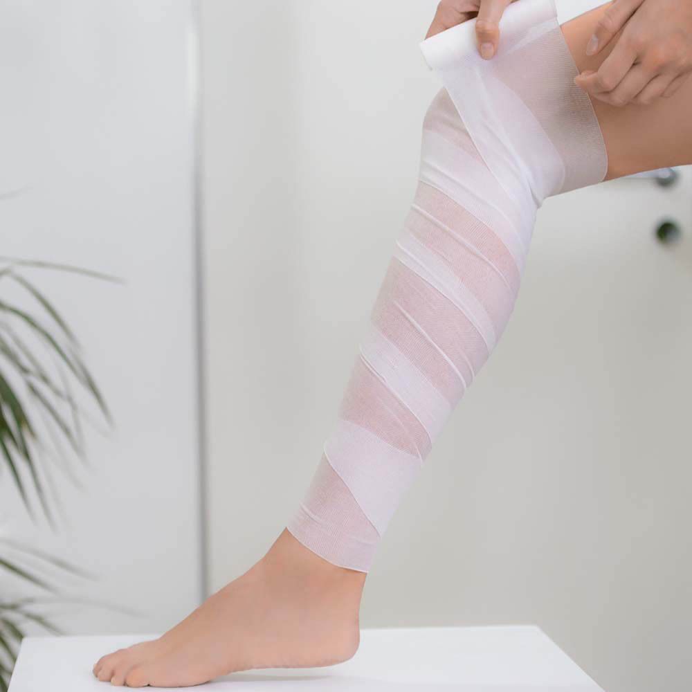 Personne enroule un bandage autour de la jambe. Bandage blanc. Marque Collistar Milano. Contient Bandes Amincissantes Drainantes.