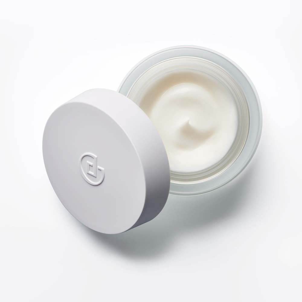 Pot de crème, couvercle ouvert. Crème visible. Couvercle blanc, récipient en verre.