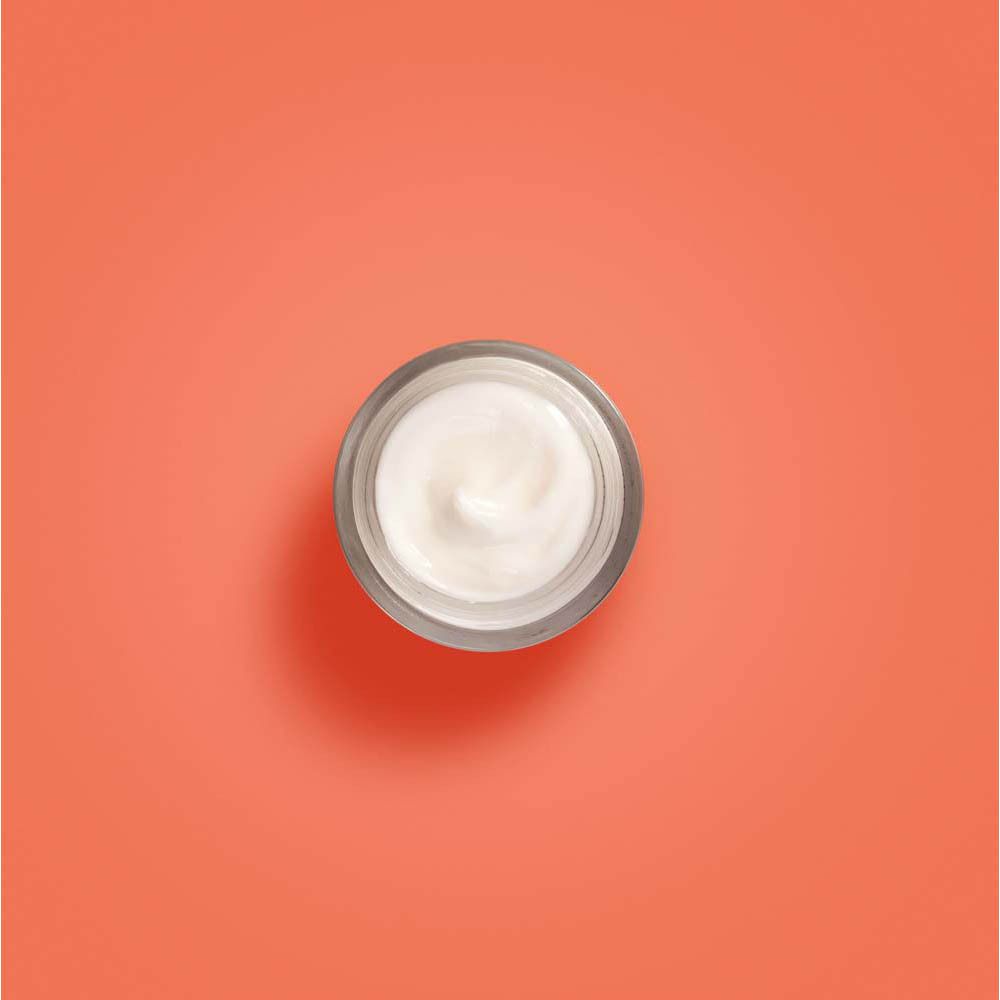 Pot de crème, vue de dessus. Crème sur fond orange. Récipient en verre.