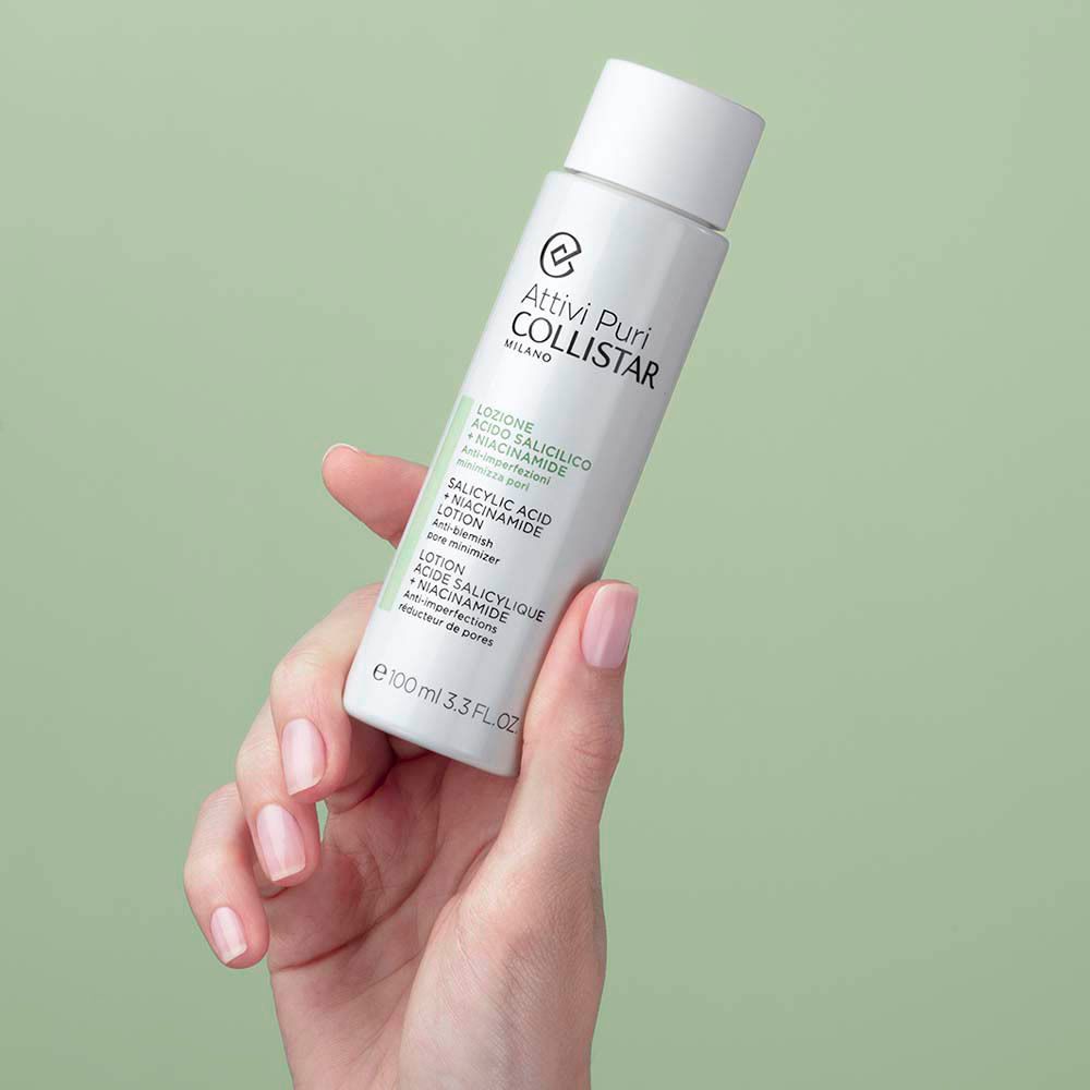 Main tenant un flacon blanc avec bouchon. Inscription : Collistar, Lotion Acide Salicylique + Niacinamide.